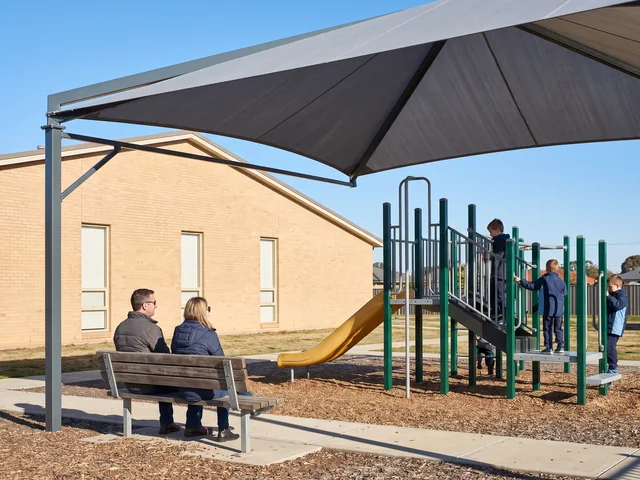 Bench under an evergreen shade frame next to a play area