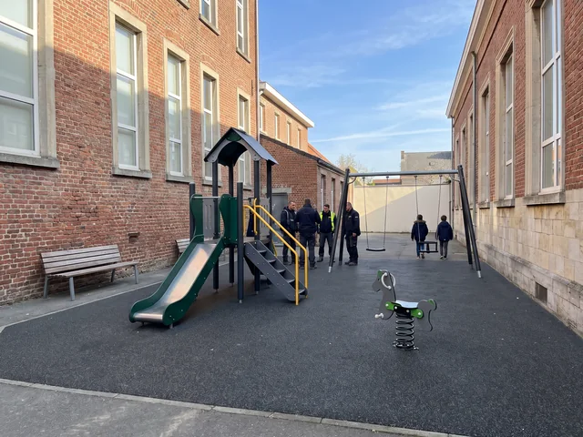 Compact play structure with a swing and a spring rider in a small courtyard between two buildings