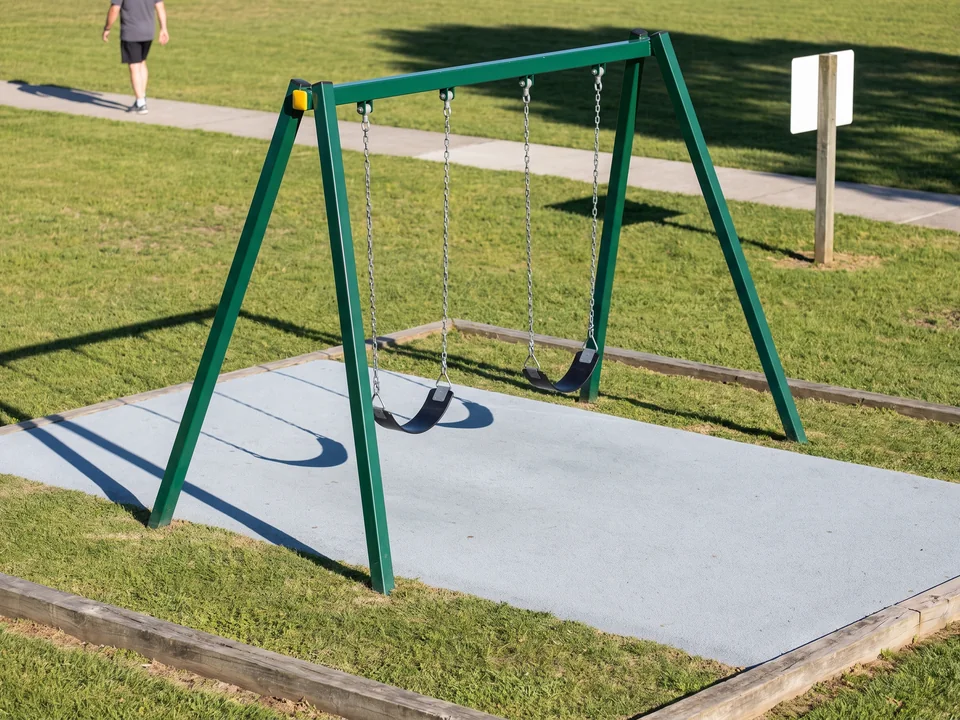 An evergreen A-frame swing set on a park lawn, its angled legs spreading at the end of the bay