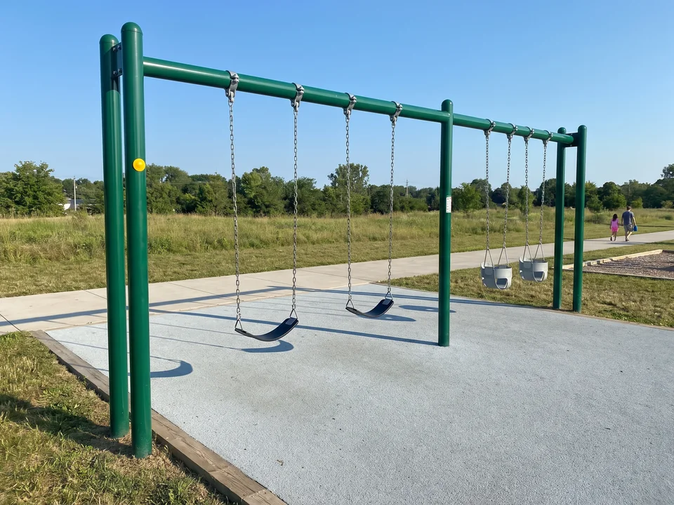 A two-bay straight-post swing frame standing beside a park path