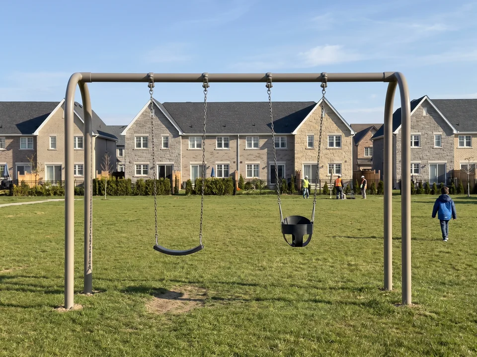Swing bay with a belt seat and a toddler bucket seat set along a community green