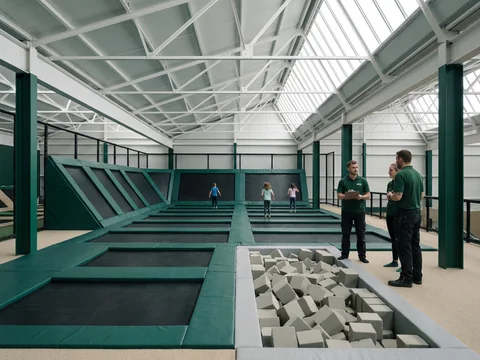 Grid of black trampoline beds with evergreen frame pads beside a light grey foam pit