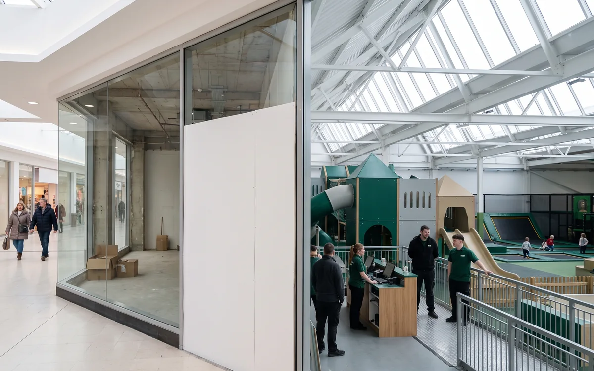 Vacant mall anchor unit with a glass shopfront facing the concourse behind site hoarding