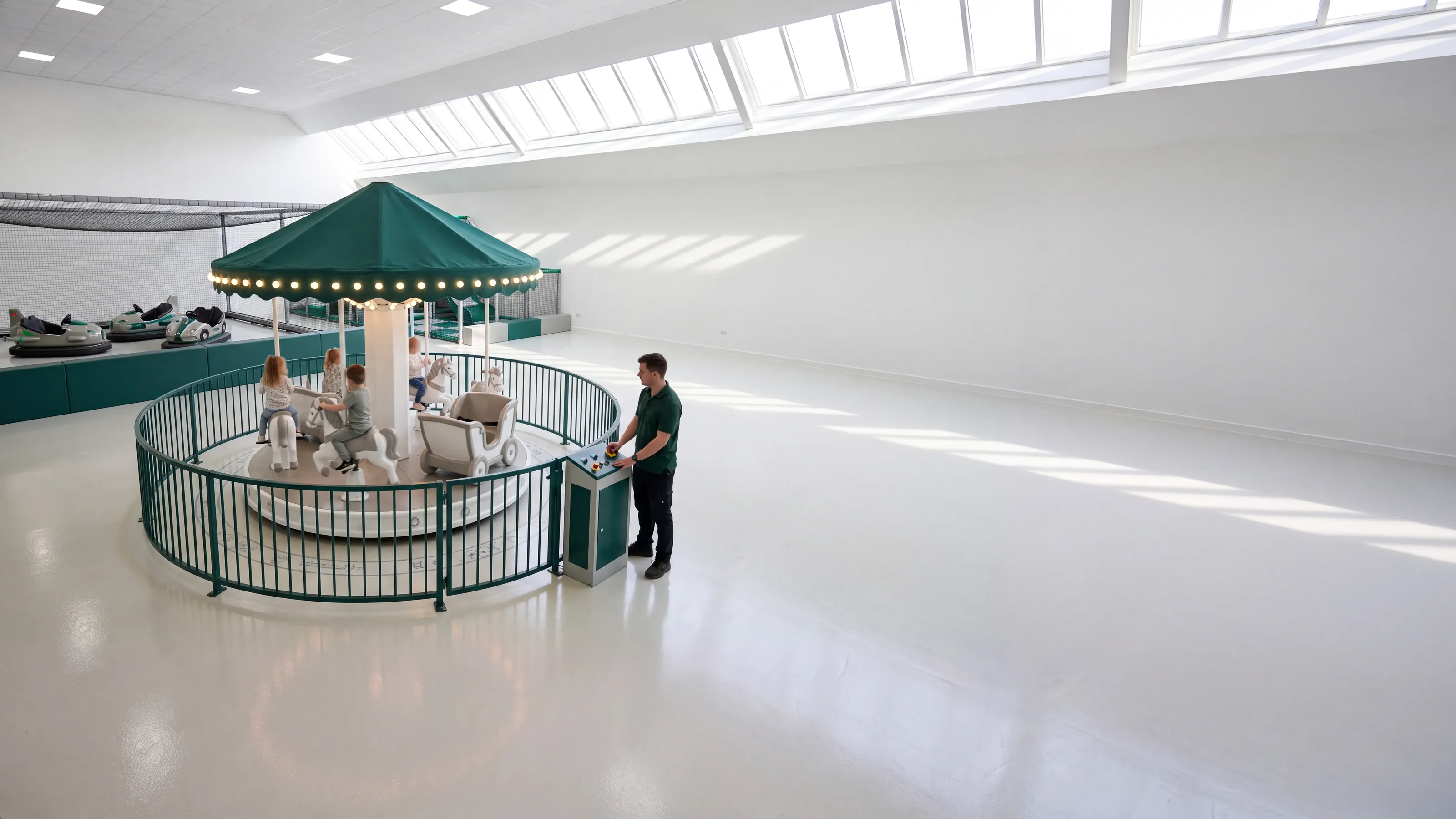 A new small electric carousel with an evergreen canopy and warm-white lights turning in a skylit family entertainment center, an operator at the control box by the fence gate
