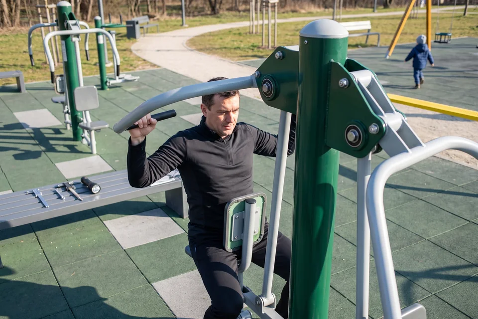 An adult uses an outdoor fitness station in a park