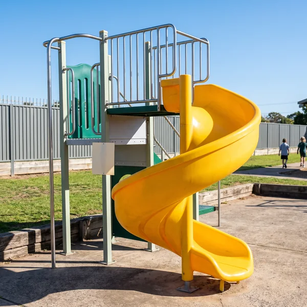 A yellow spiral slide turning down from the tallest deck of a play structure