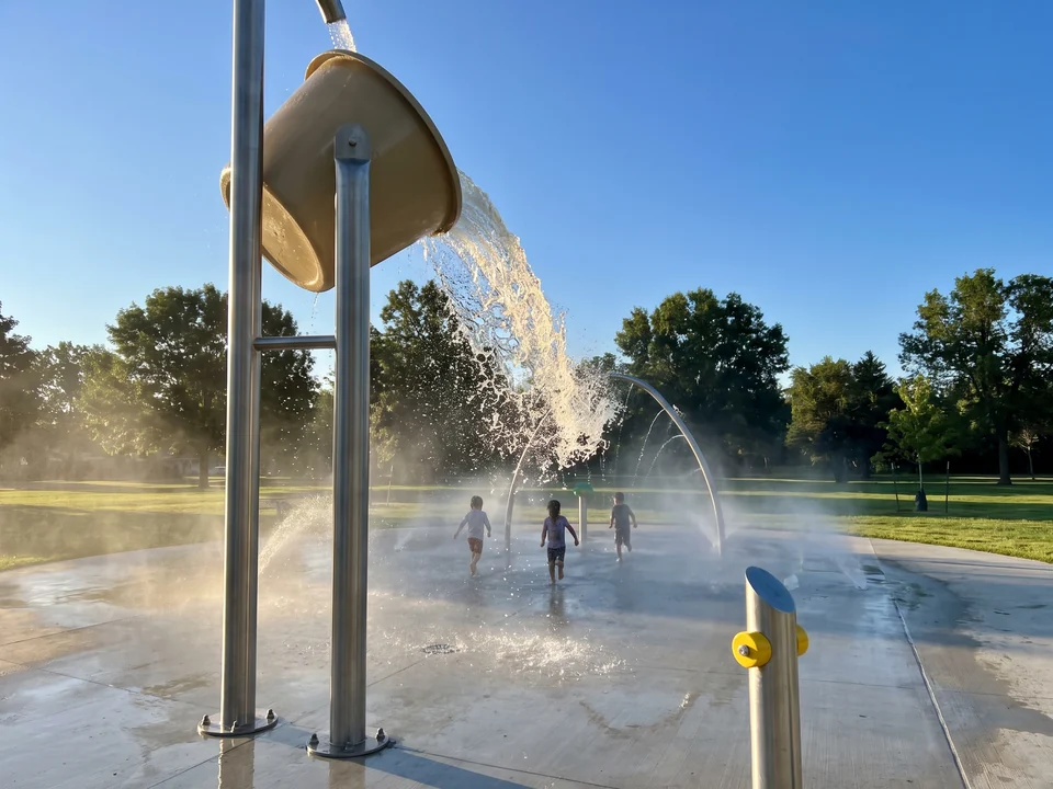 A tipping bucket on a stainless post spilling water, lit from behind