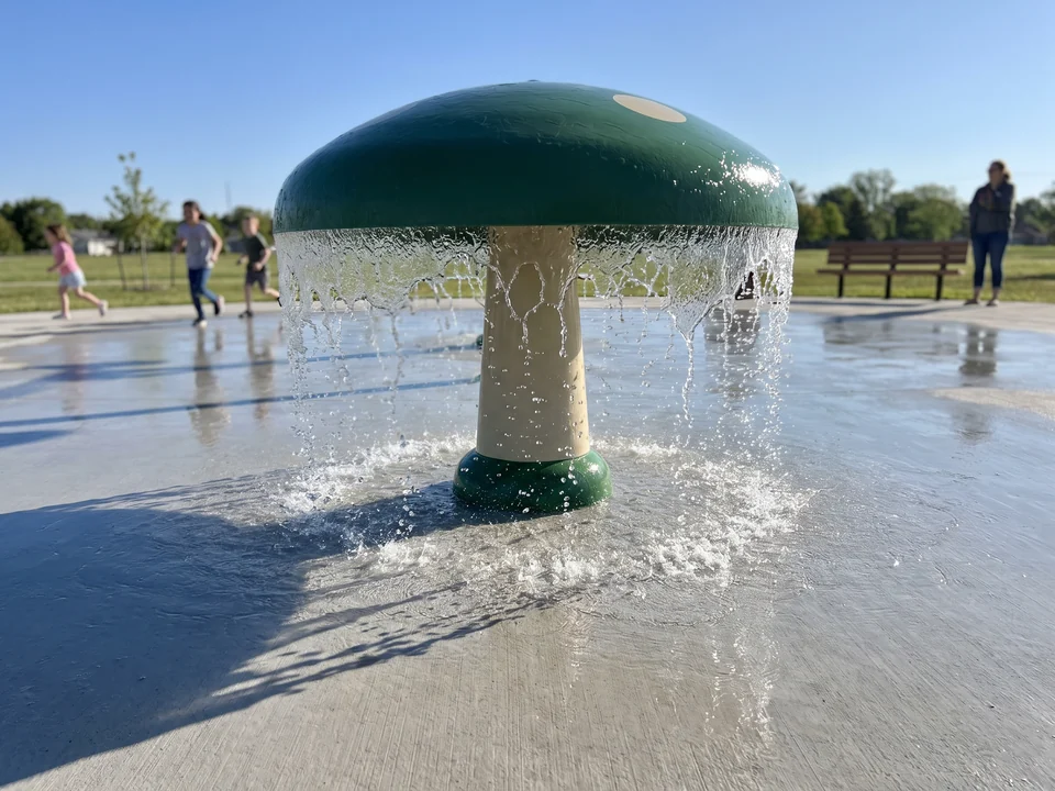A realistic two-color fiberglass mushroom sprayer on a splash pad with water falling from the cap edge