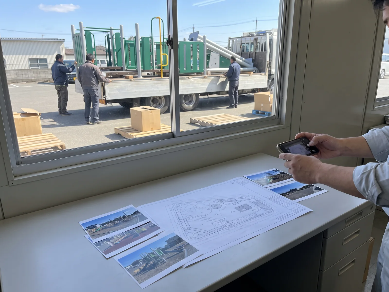 At a dealer's office, a printed site plan and site photos are laid out on a desk and photographed with a phone